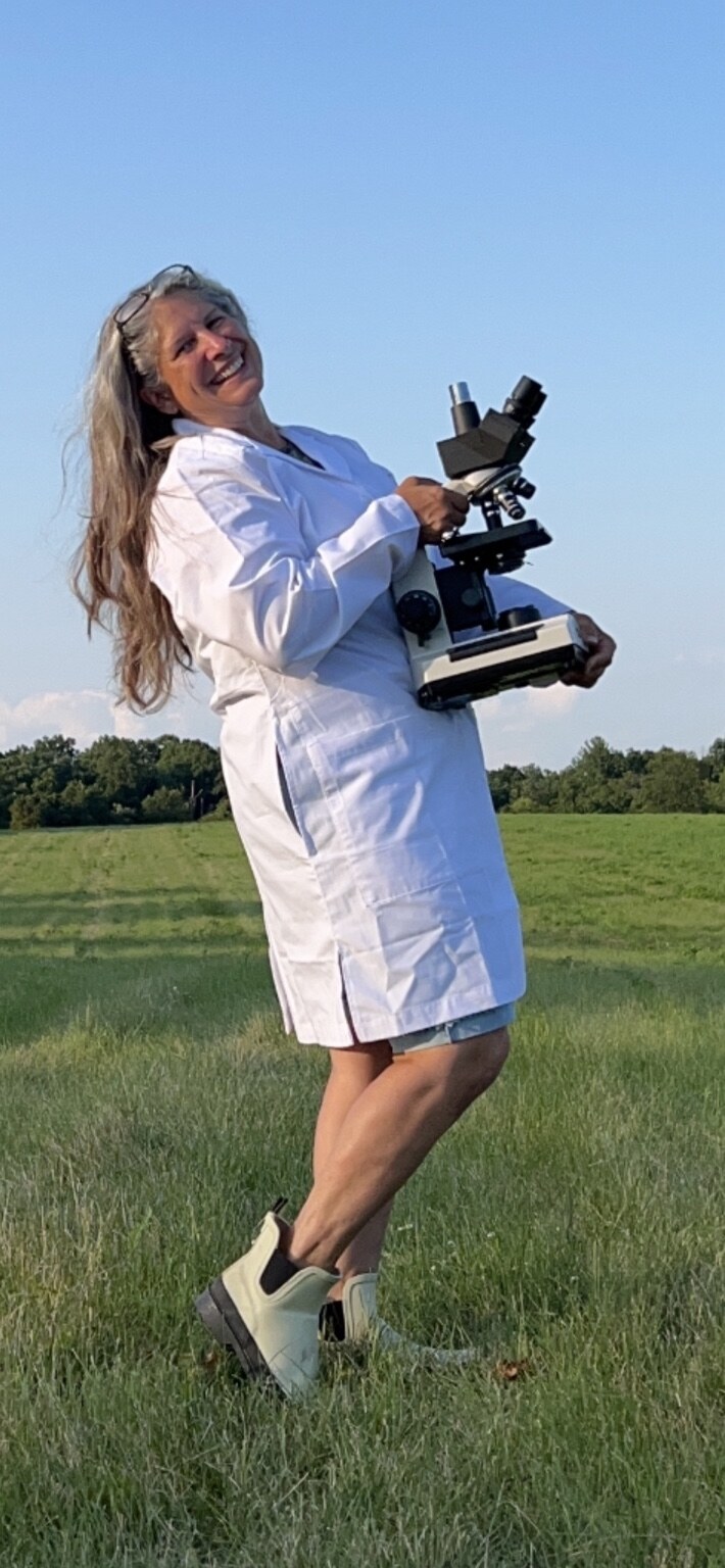 Suzanne L. Shea standing in a field while holding a microscope